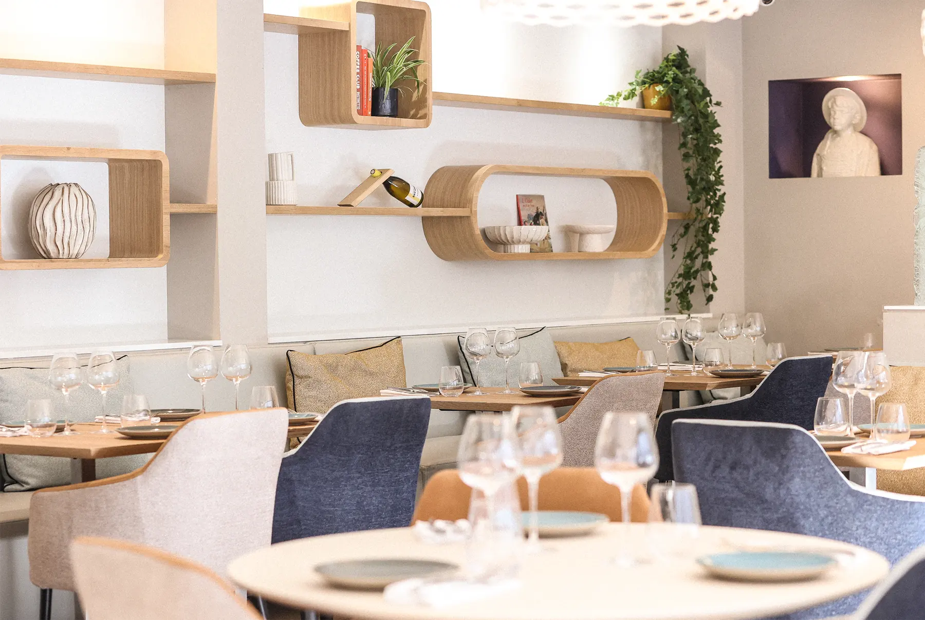 La nouvelle salle du Prieuré et pas que : étagères en bois clair, banquette, fauteuils bleu nuit et beiges, tables dressées